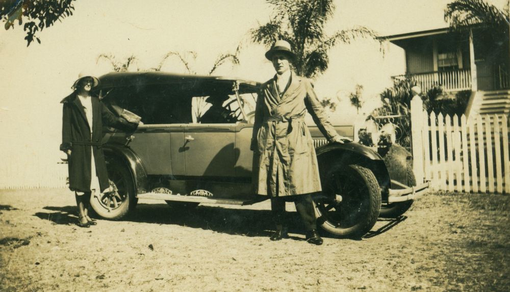 Standing near a car outside a house, ca. 1920s