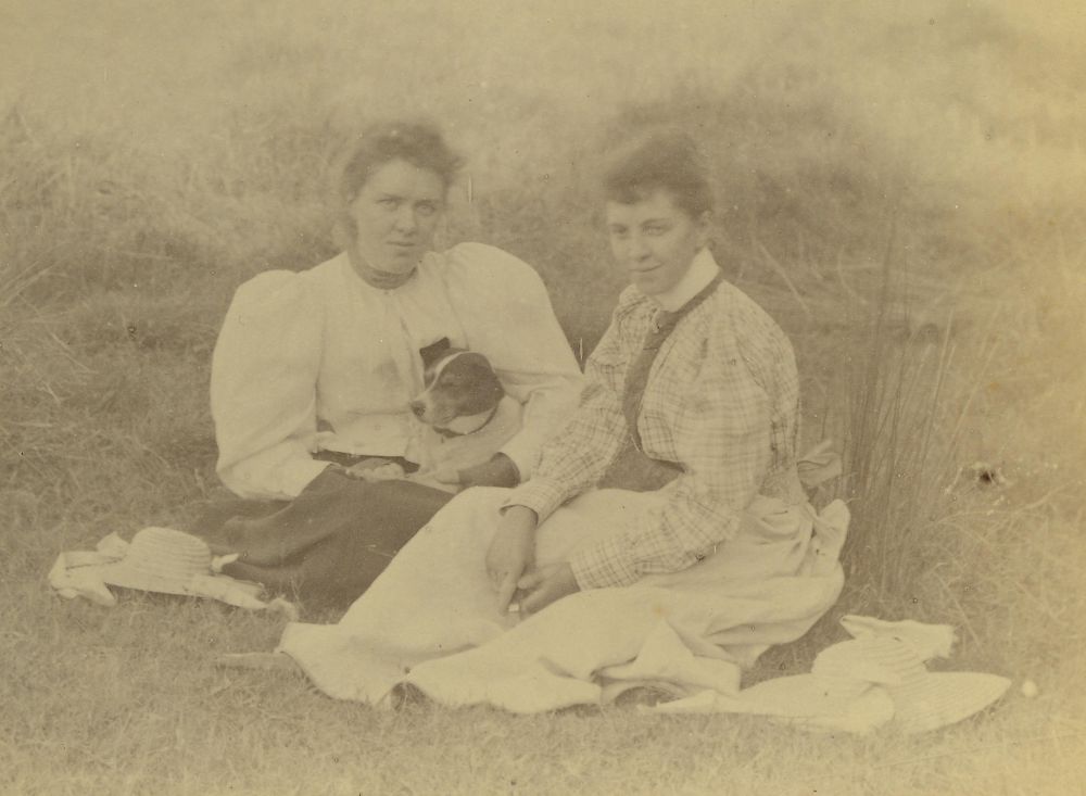 Two women sitting on the grass with their dog