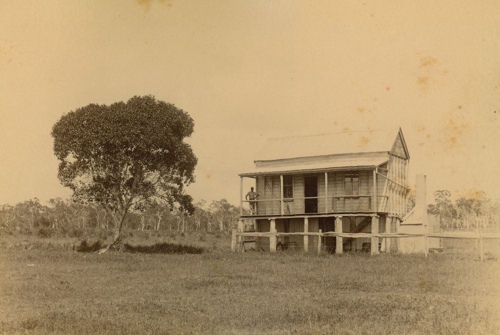 Small two storey house with a man standing on the verandah