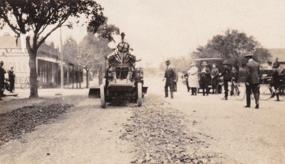 Man driving a grader down main street of a town, ca. 1930