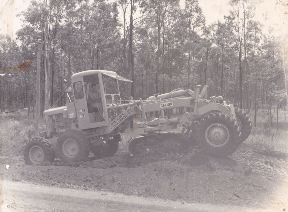 Bill Neller driving a grader owned by Pine Rivers Shire Council, ca. 1960