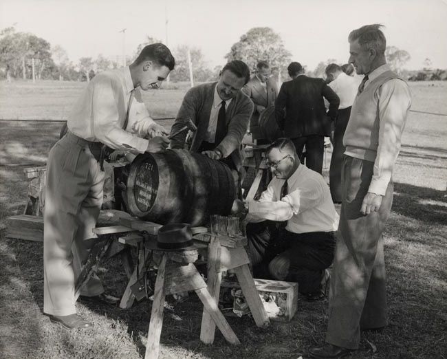 Staff drawing beer for men from kegs set up under trees