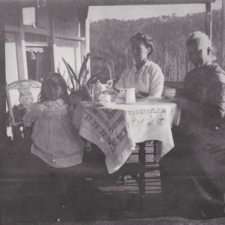 Two women and a young girl sitting at a table on a verandah